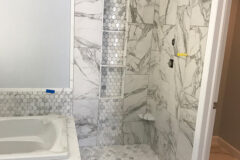 Shower Wall: 12′′ × 24′′ Porcelain tile, vertical subway pattern, with quartz shelf and quartz curb. Backsplash: 2′′ × 2′′ Hexagon marble with custom-cut quartz edge. Tub Deck: Quartz. Shower Niche: 2′′ × 2′′ Hexagon marble with three quartz shelves, in Thornton, Colorado