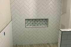 Shower Wall: 4′′ × 8′′ Ceramic tile, herring bone pattern. Niche: Marble mosaic tile with Schluter edges. Bathroom Floor: 6′′ × 24′′ Porcelain tile, subway pattern, in Centennial Colorado