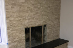 Wall: Travertine ledger (stacked stone). Hearth: Leathered black granite (chiseled edge), in Littleton, Colorado